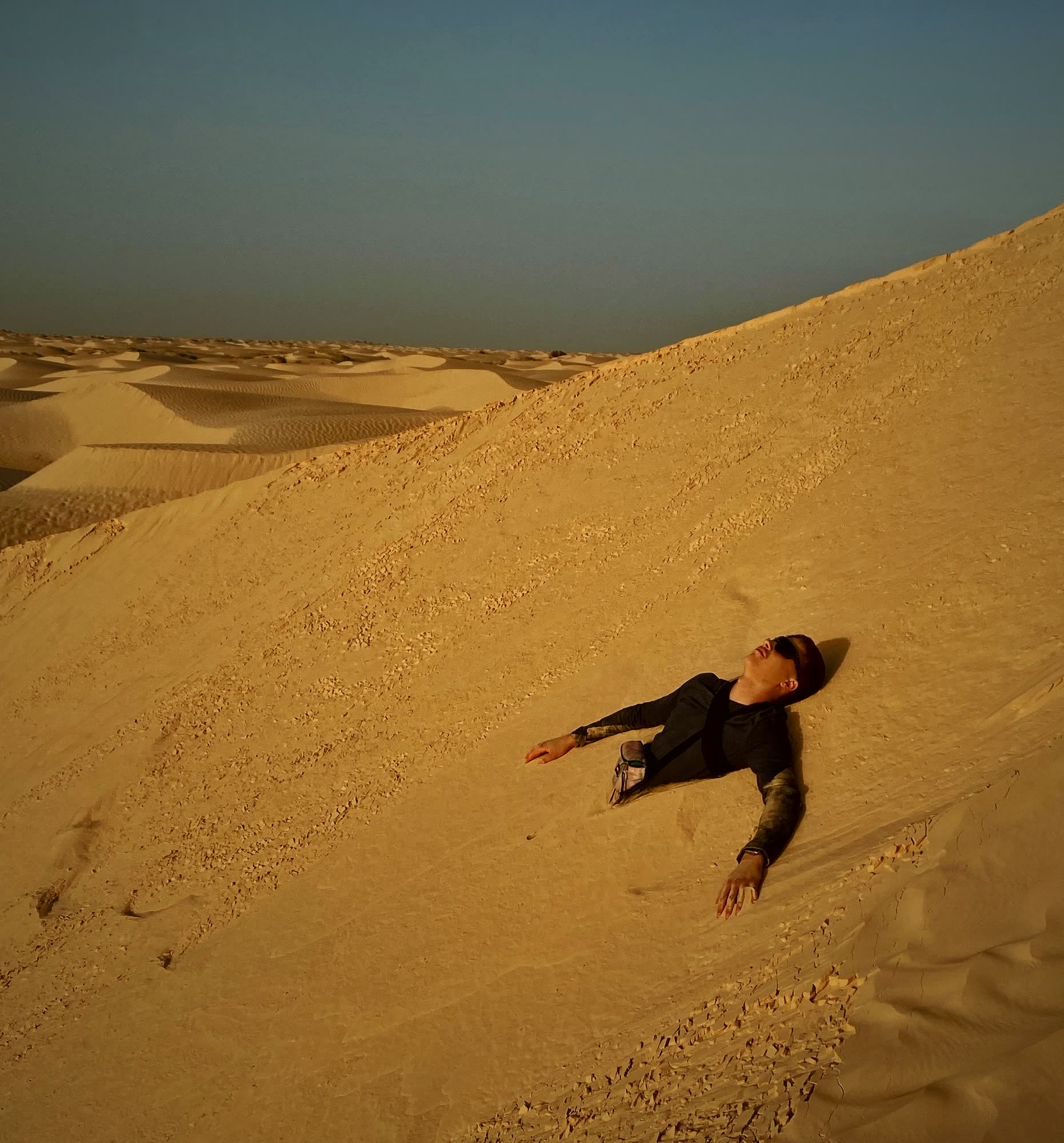 Someone lying back in a Sahara dune, arms spread, face to the sky